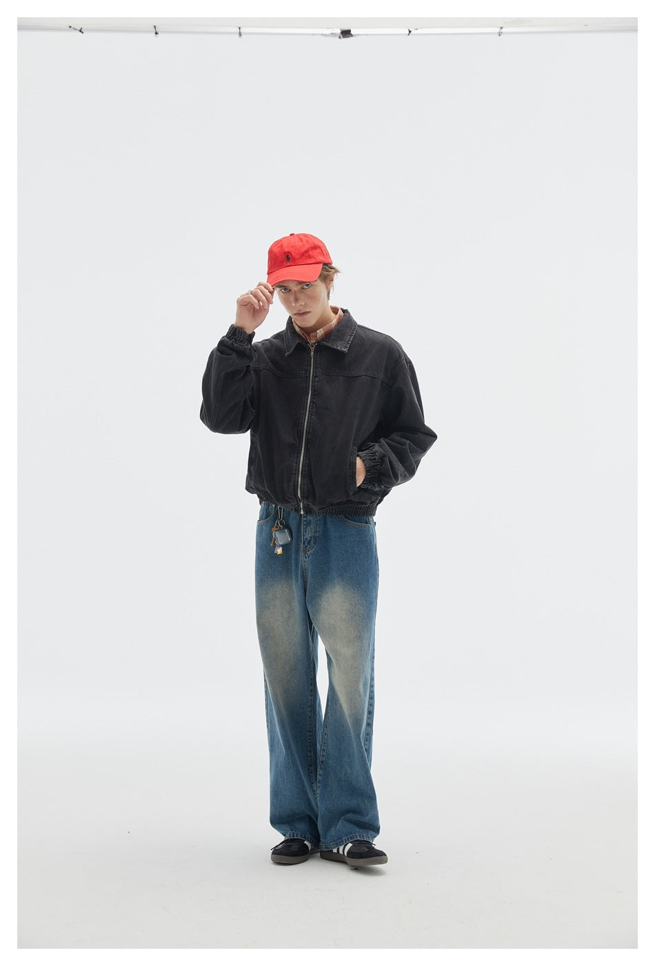 Model wearing a black zip-front jacket with gathered cuffs and hem, blue jeans, and a red cap.
