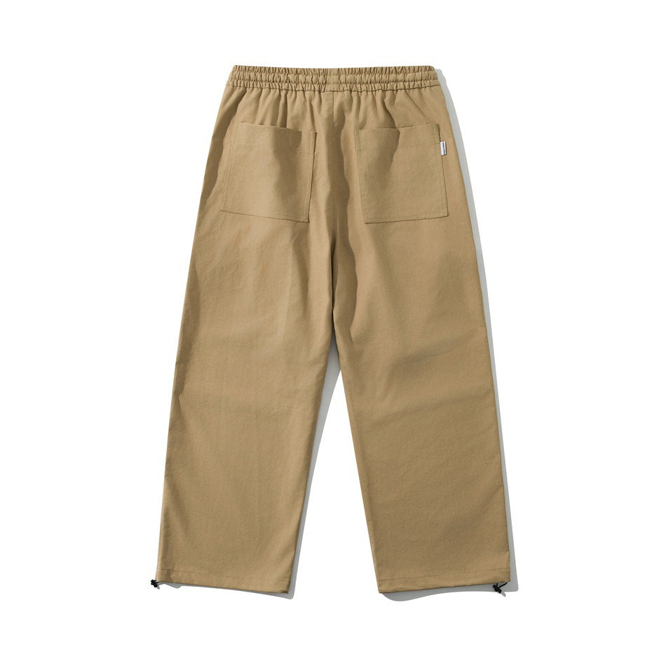 Back view of tan loose-fit pants with an elastic waistband, two patch pockets, and adjustable ankle hems.