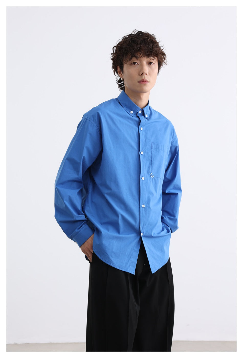Model wearing a bright blue button-down shirt with a chest pocket and black trousers.