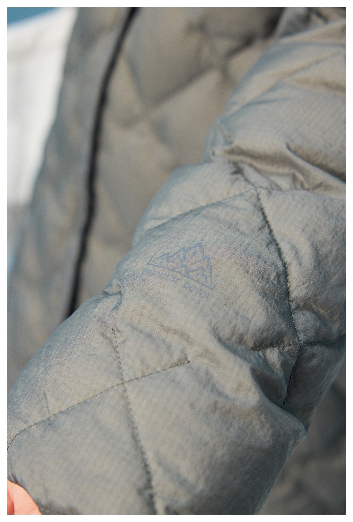 Close-up of the gray coat's diamond quilting and a small mountain emblem with the words “Premium Down.”