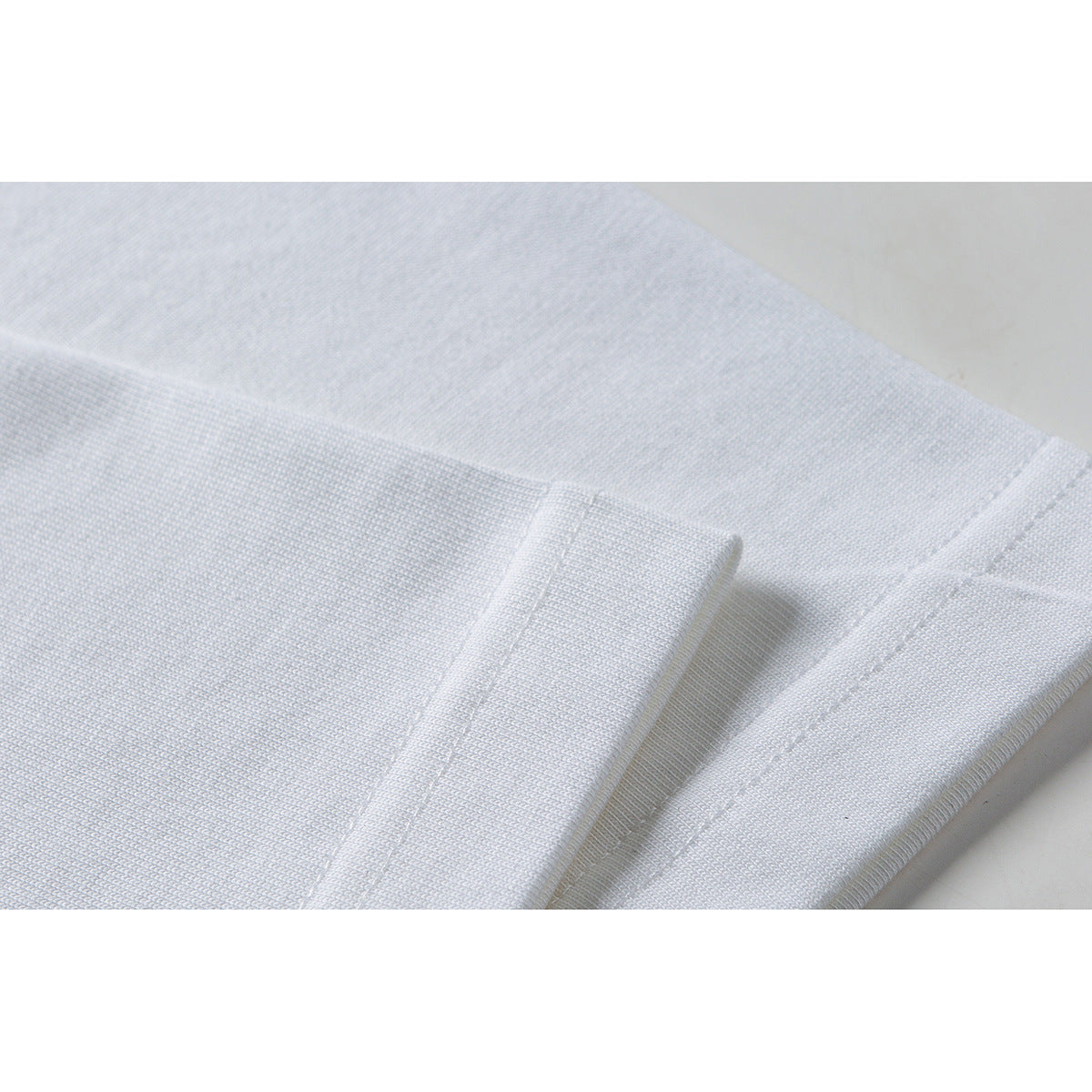 Close-up of white T-shirt fabric, folded edge, and stitched seam.