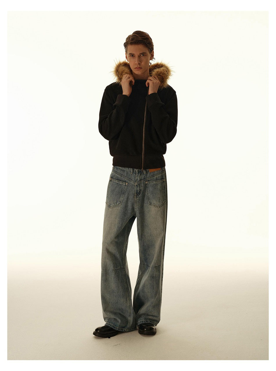 Front view of a model holding the fur-trimmed hood of a black zip-front jacket, with loose blue jeans.