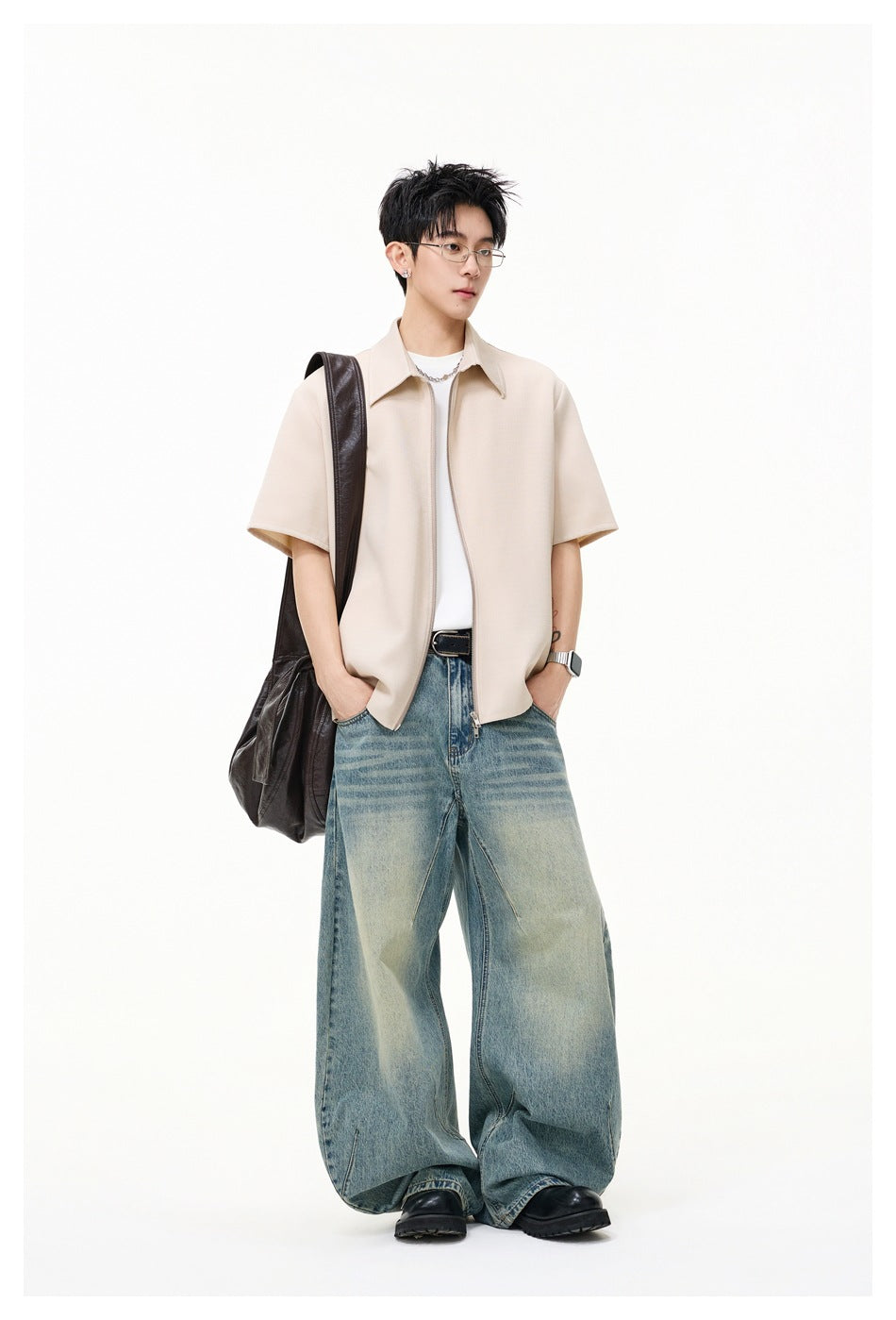 Model wearing a light beige short-sleeve zip-front collared shirt over a white tee with loose blue jeans.
