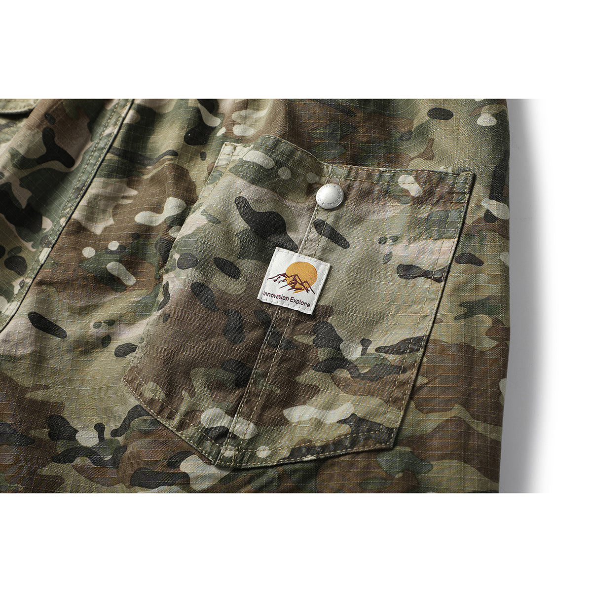 Close-up of a camouflage trouser cargo pocket with a snap closure and a small sewn-on label.