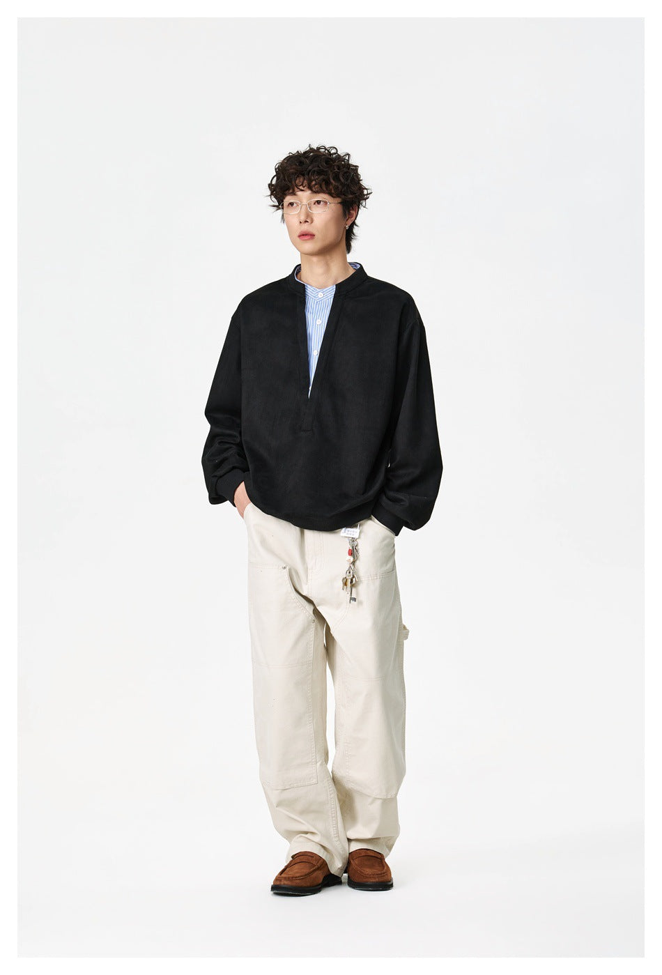 Model wearing a black loose-fit pullover with a split neckline over a blue-and-white striped shirt.