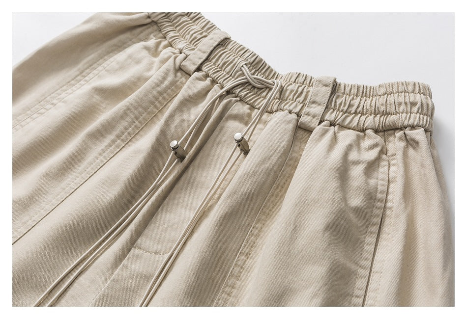 Close-up of beige shorts showing the elastic waistband, long drawstrings, toggles, and front seams.