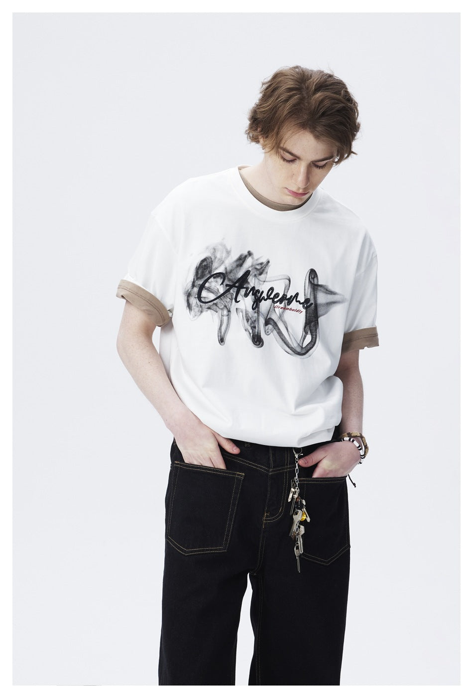 Close-up of model wearing white smoke-print graphic T-shirt with rolled beige undershirt sleeves and black jeans