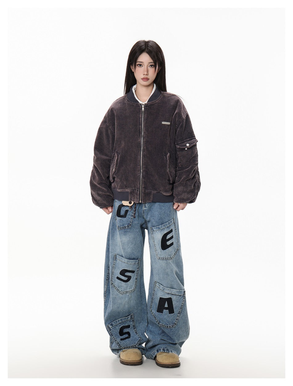 Front view of a model in a zipped dark brown ribbed bomber jacket and oversized letter-patch jeans.