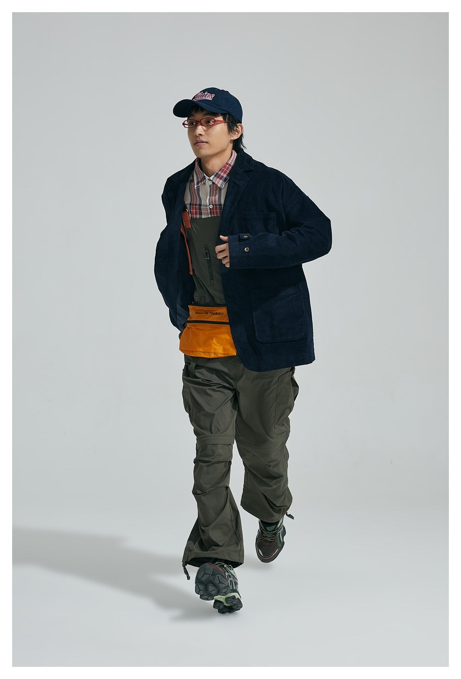 Full-length model wearing a dark navy ribbed blazer with patch pockets, plaid shirt and olive cargo trousers.