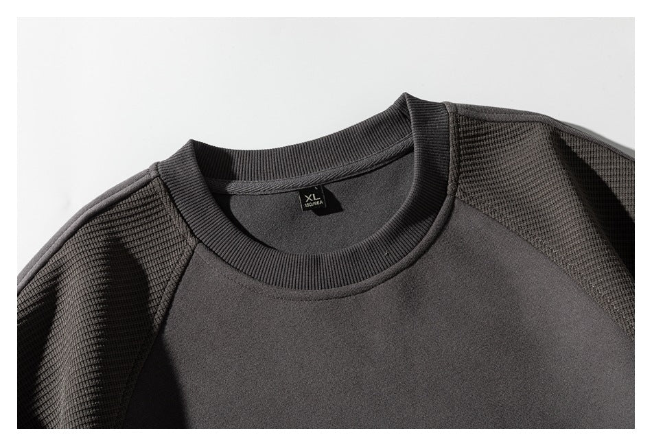 Close-up of a charcoal crewneck sweatshirt showing its ribbed collar, textured shoulder panels and XL neck tag.