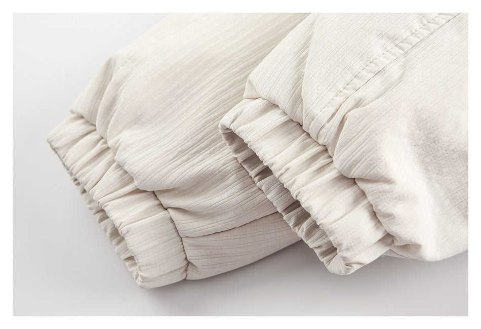 Close-up of an ivory quilted garment with softly gathered, narrow-ribbed panels.