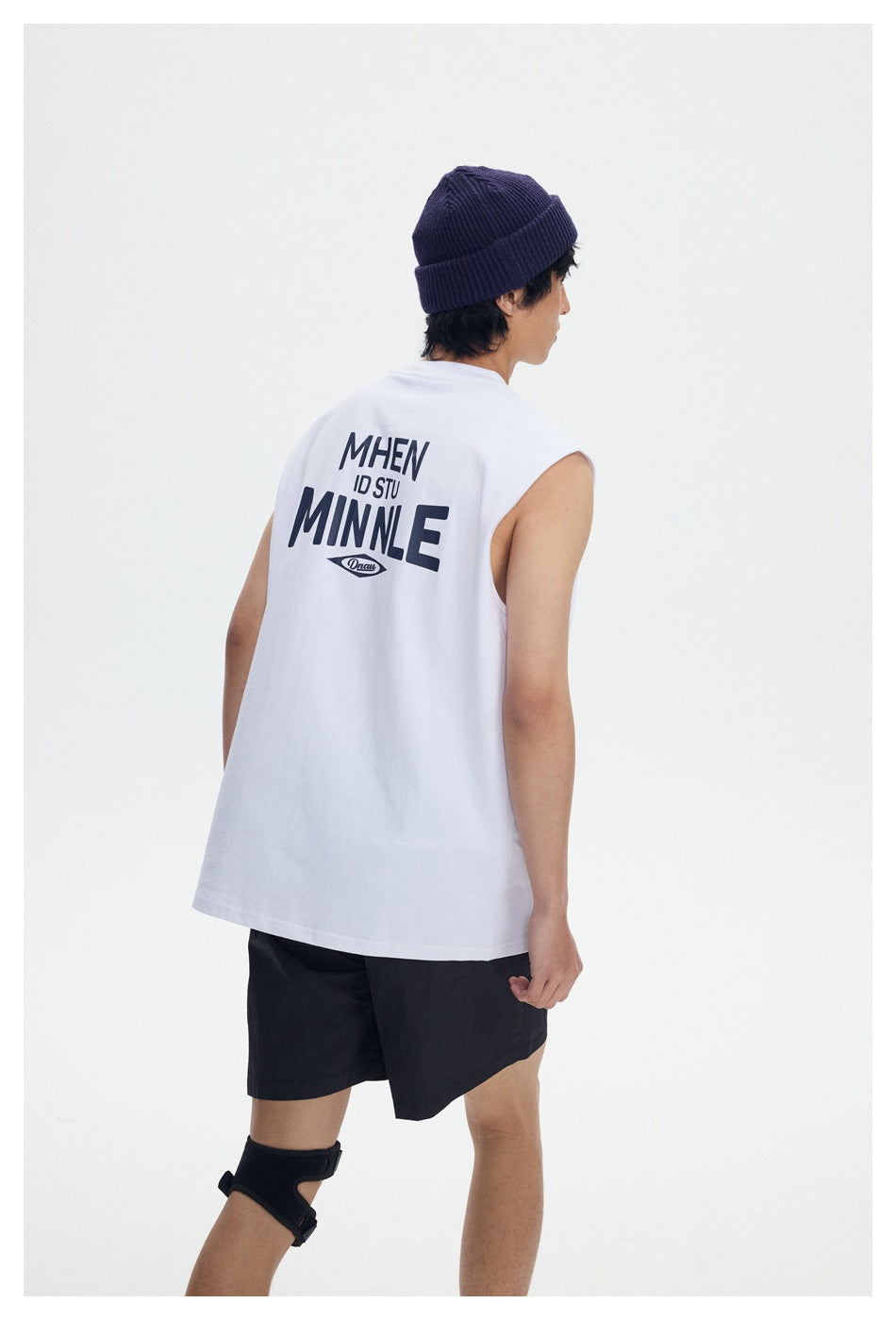 Rear view of a model wearing a white sleeveless shirt with large dark back lettering and black shorts.