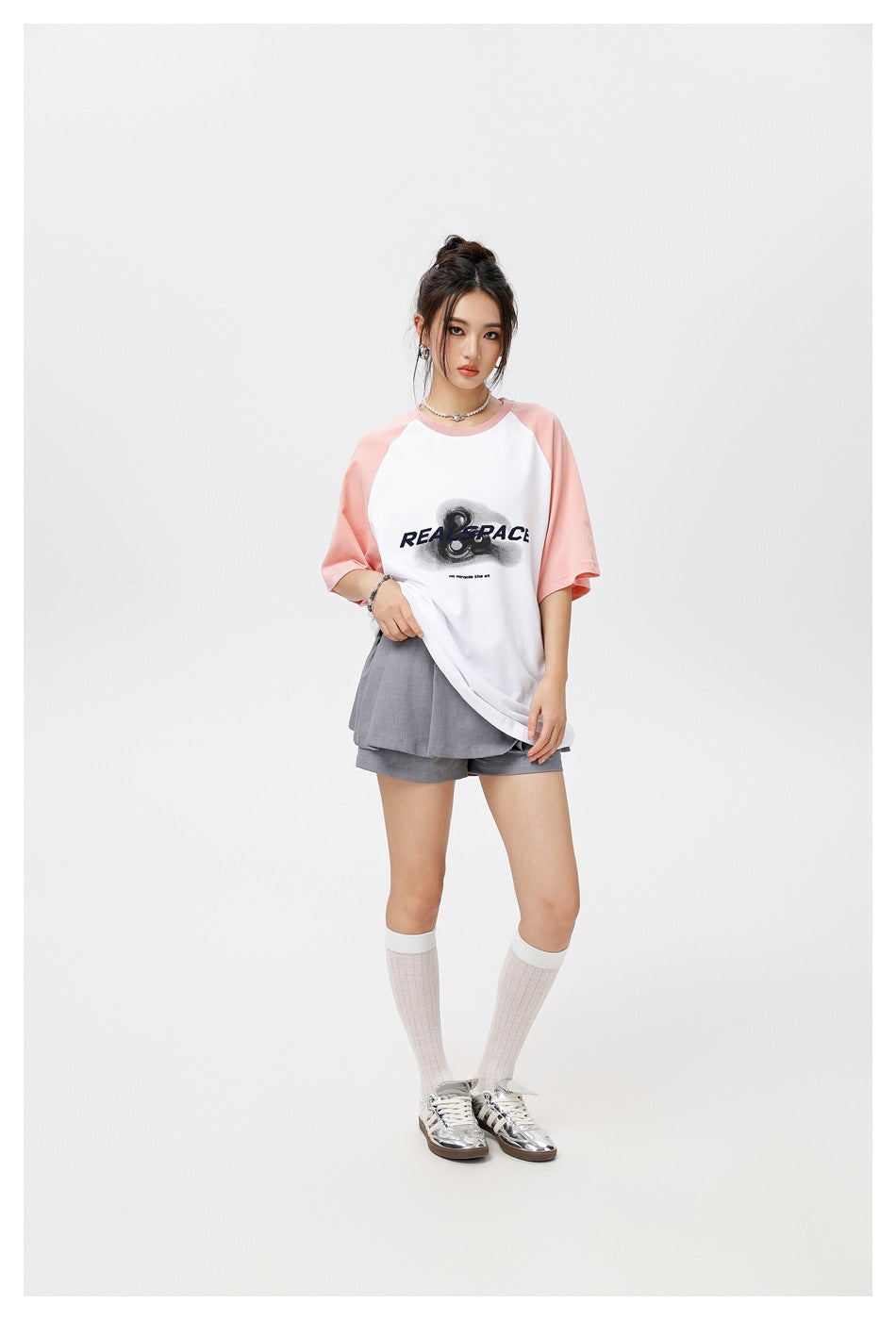 Model wearing the pink and white raglan T-shirt with gray pleated shorts, white knee socks and silver sneakers