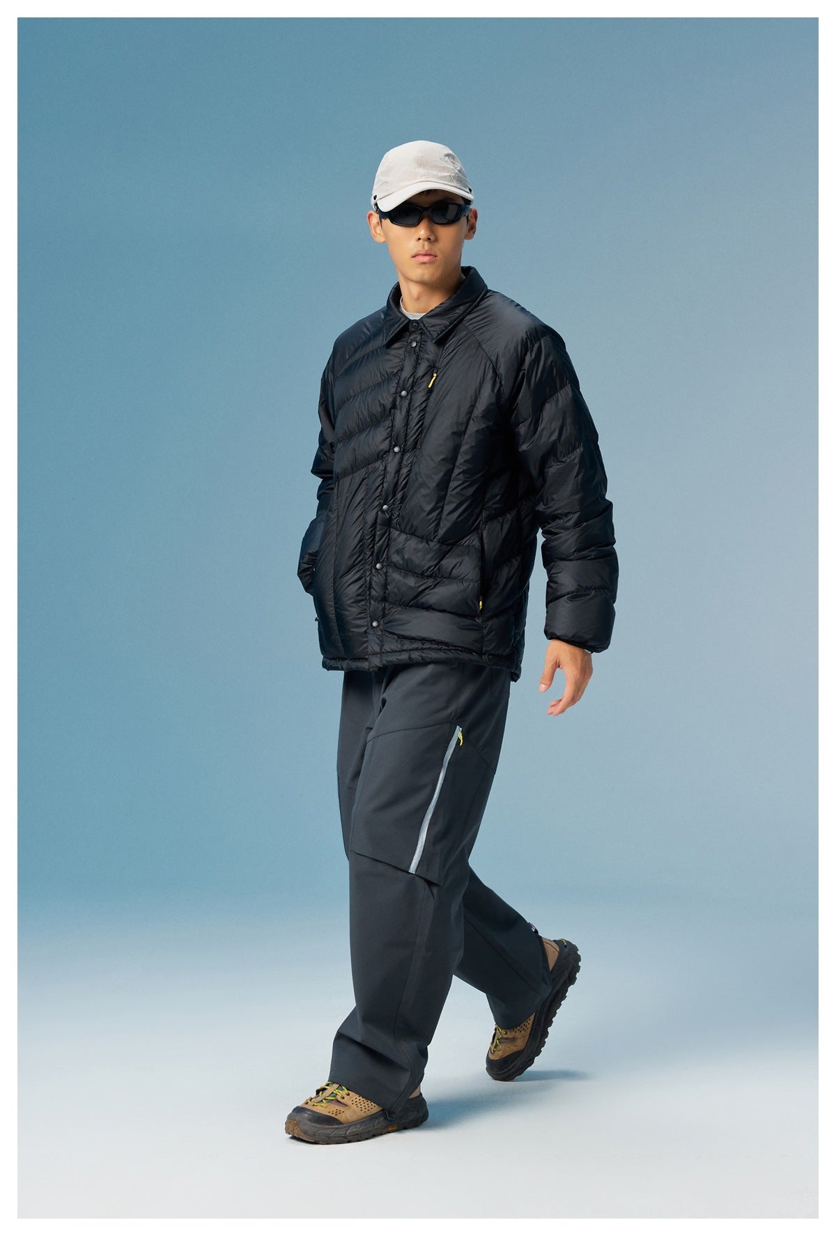 Front view of a model wearing a black quilted puffer jacket with a collar, snap front, and yellow zipper detail.