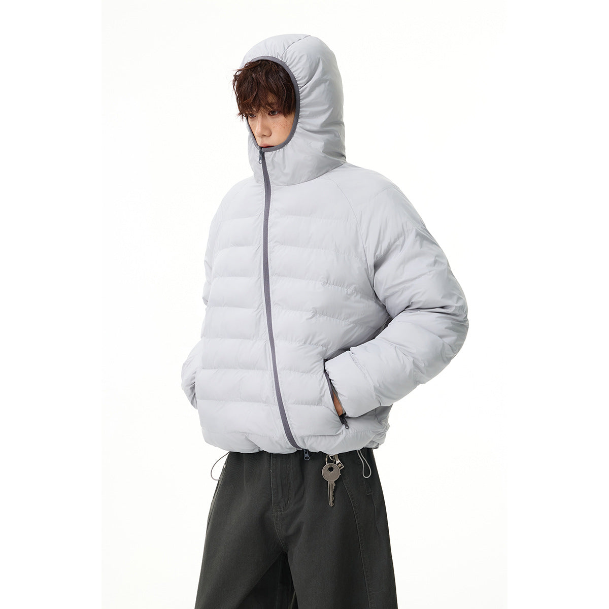 Model wearing a light gray quilted hooded jacket with dark gray zipper trim and dark trousers.