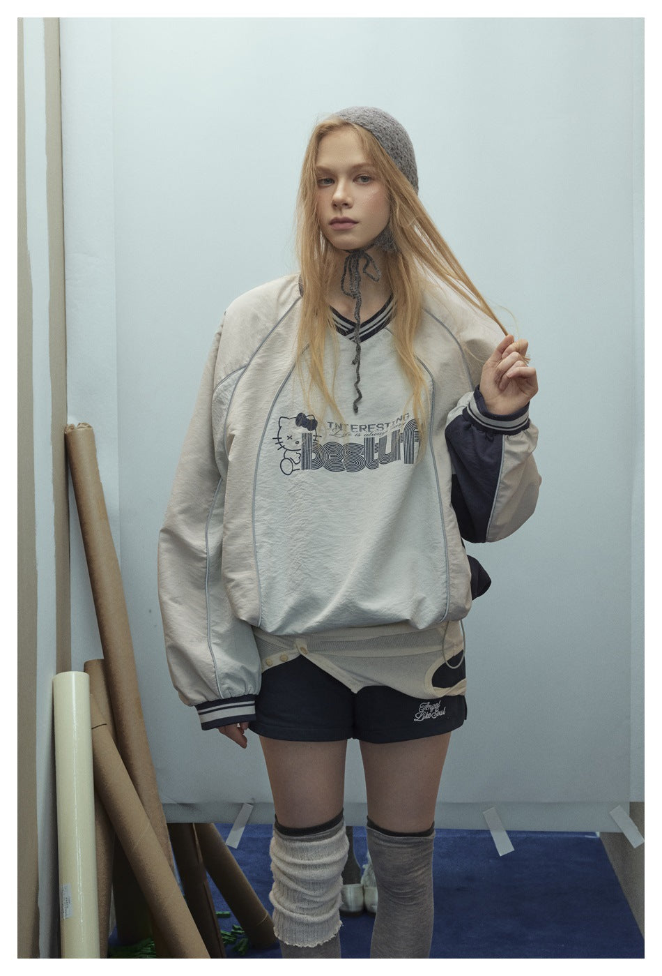 Model wearing an oversized cream sweatshirt with dark sleeve panels, contrast piping and a chest graphic, viewed from the