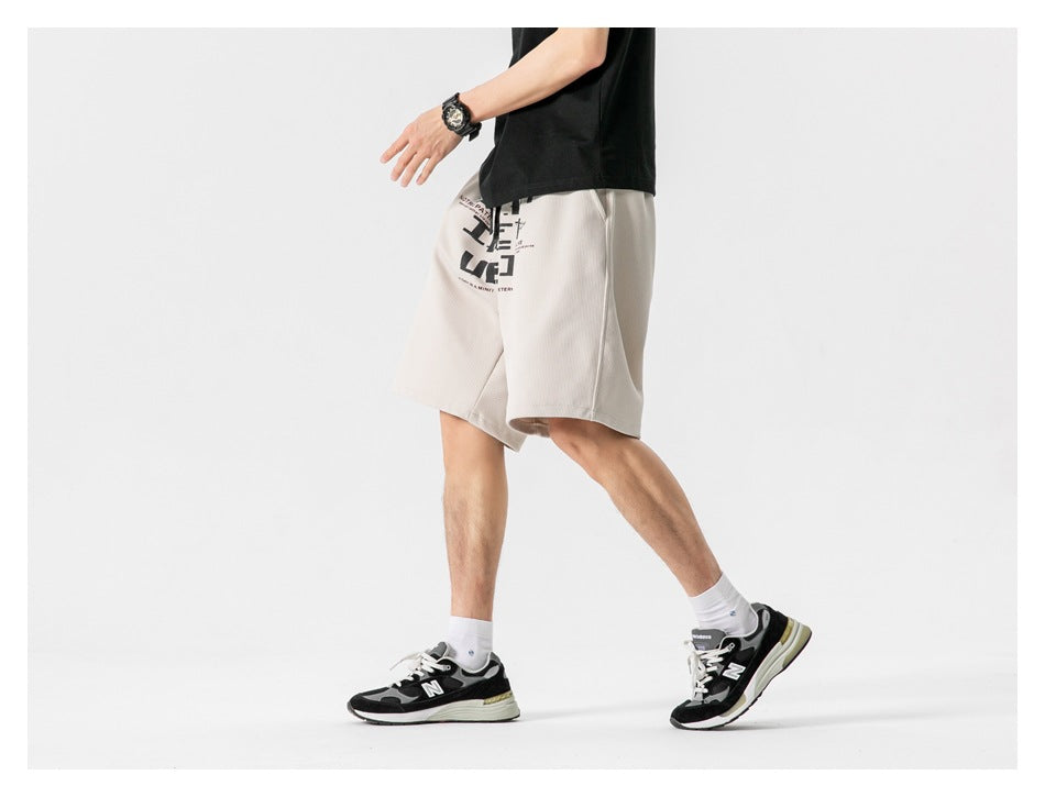 Cropped side view of a model wearing light beige knee-length shorts with a black graphic print.