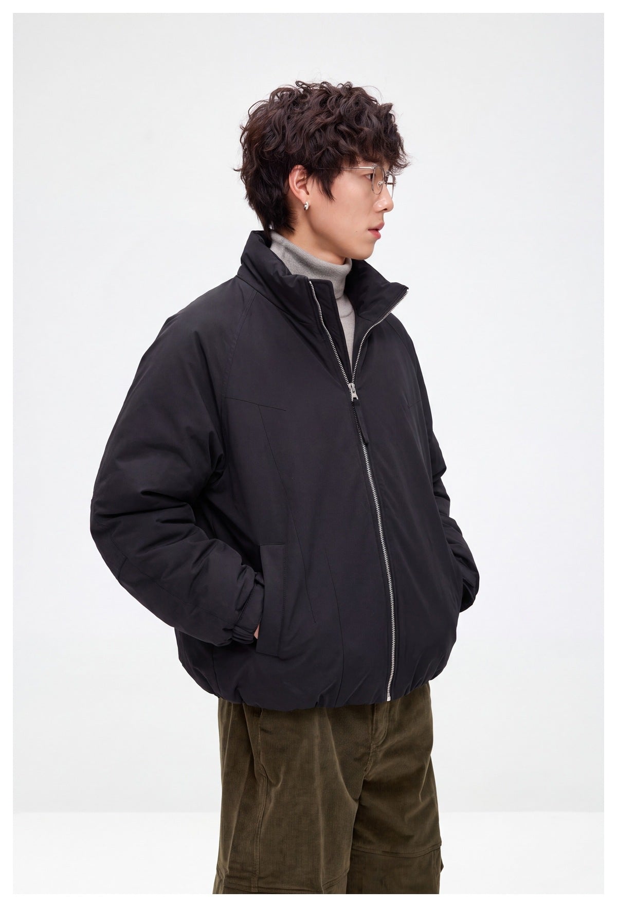 Side view of a model wearing a black zip-front jacket with a tall collar and side pockets.