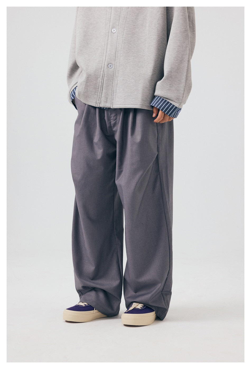 Cropped front view of a model wearing loose gray trousers with a light gray jacket and striped cuffs.