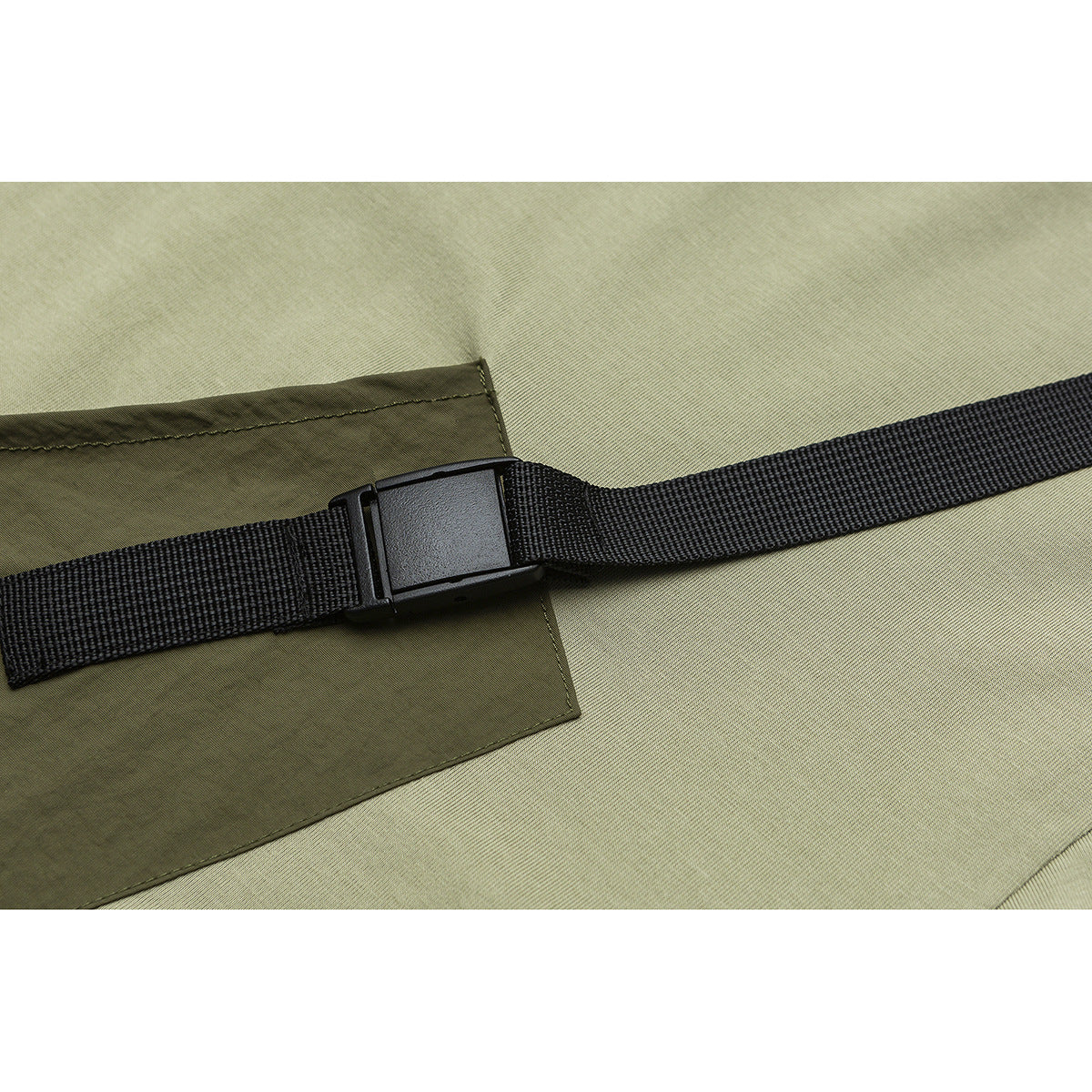 Close-up of a black webbing strap and plastic buckle crossing an olive-green garment pocket.