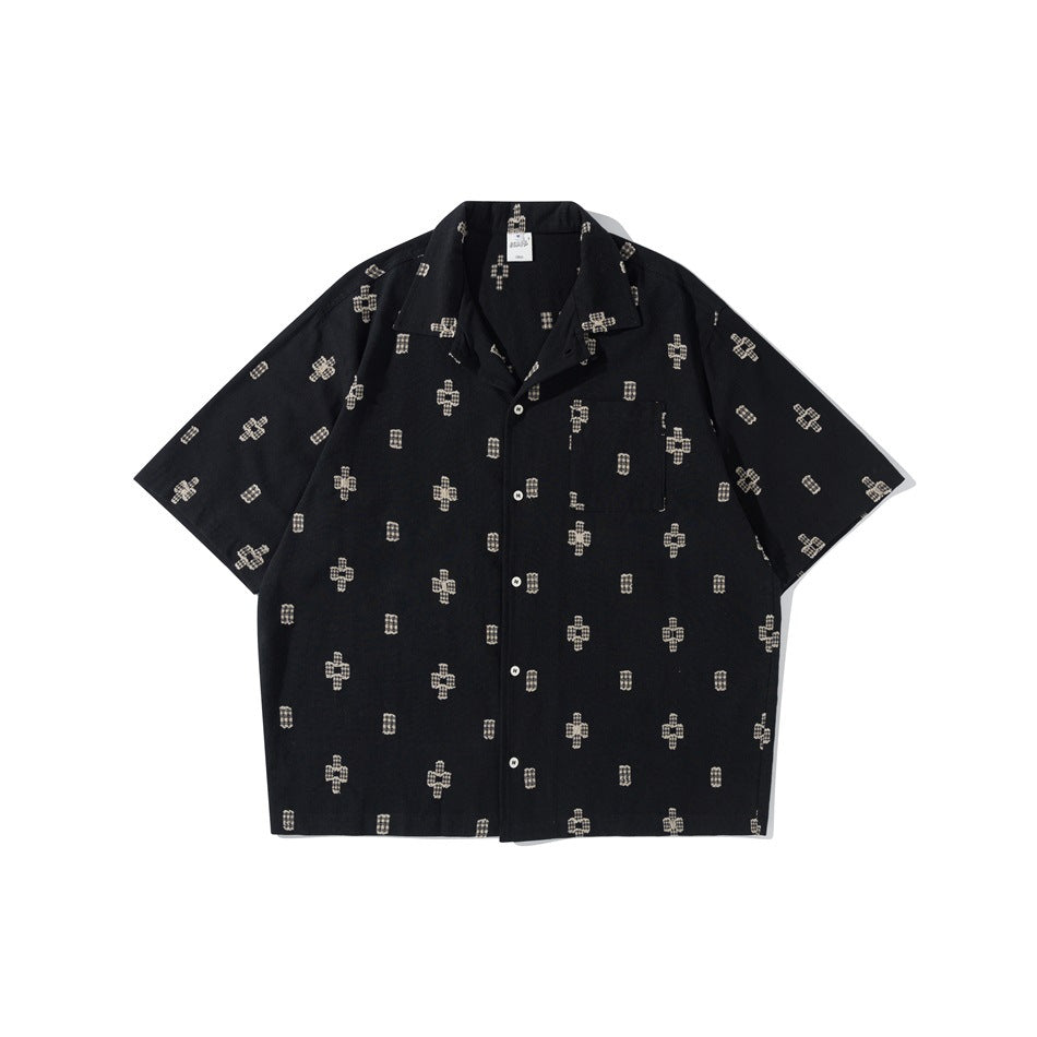Black short-sleeve camp-collar shirt with cream cross and rectangle motif, chest pocket and buttons, flat lay