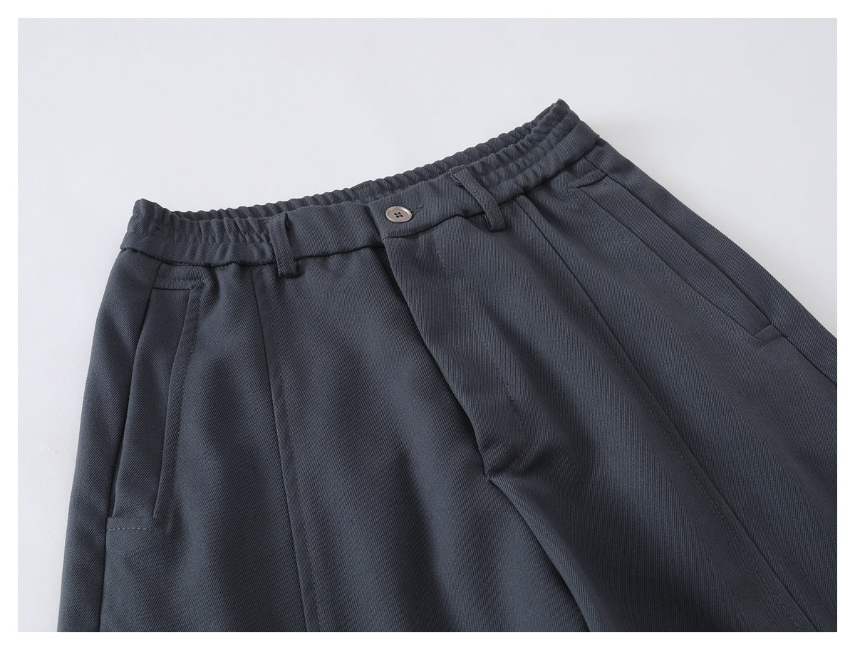 Close-up of charcoal wide-leg trousers showing the elasticated waistband, button closure, pleats and front pockets.