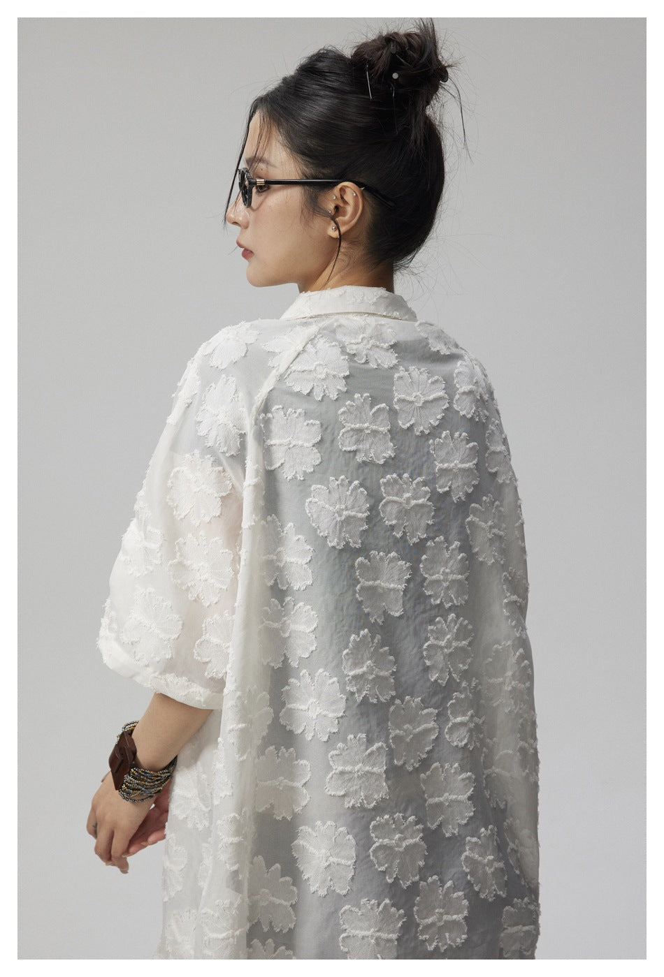 Back view of a model wearing a white sheer floral shirt with raised flower details.