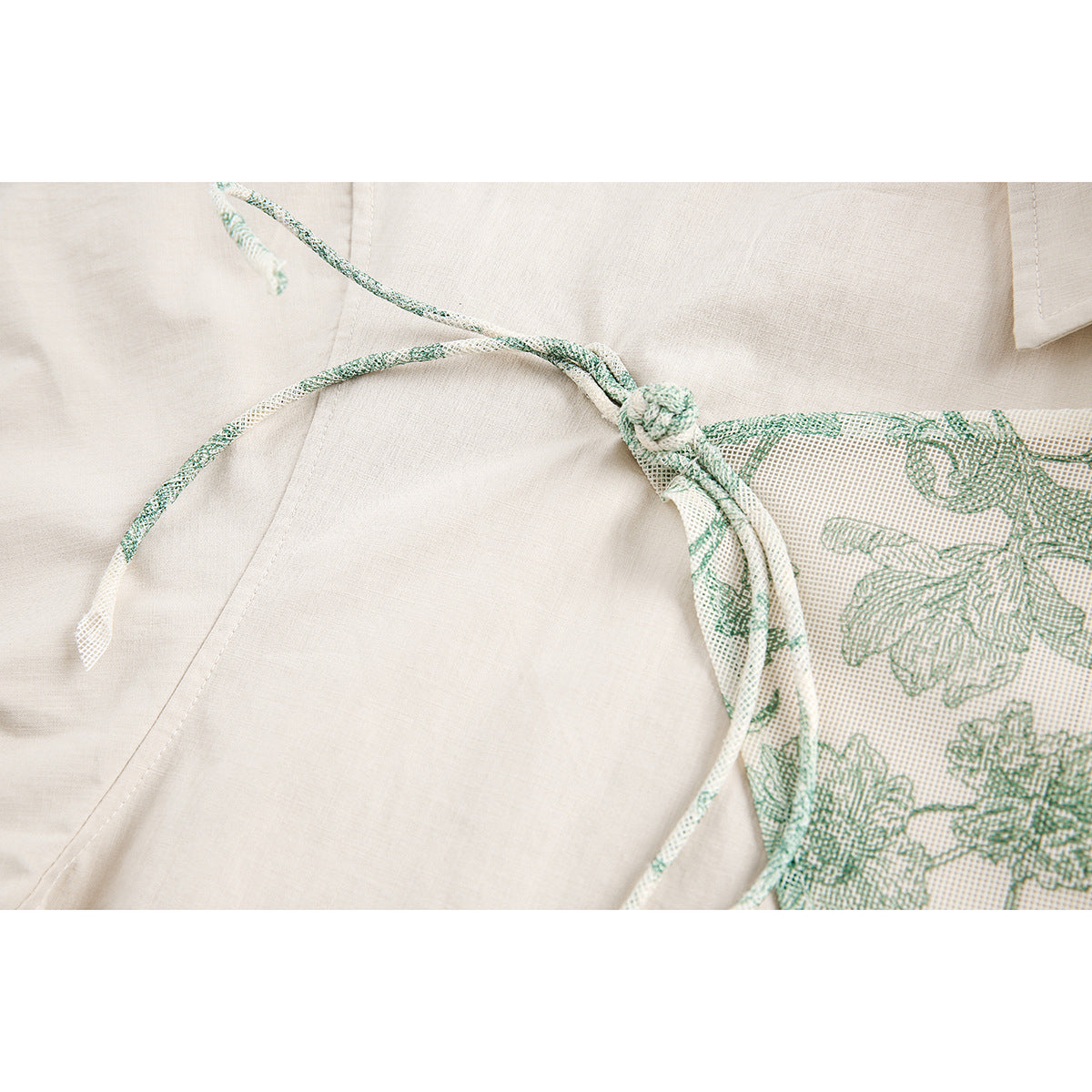 Close-up of cream shirt fabric with green floral print and a knotted matching cord.