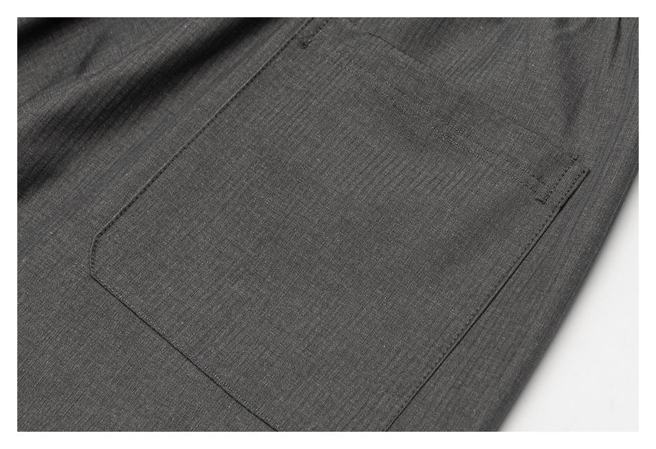Close-up of a stitched patch pocket on dark gray trousers.