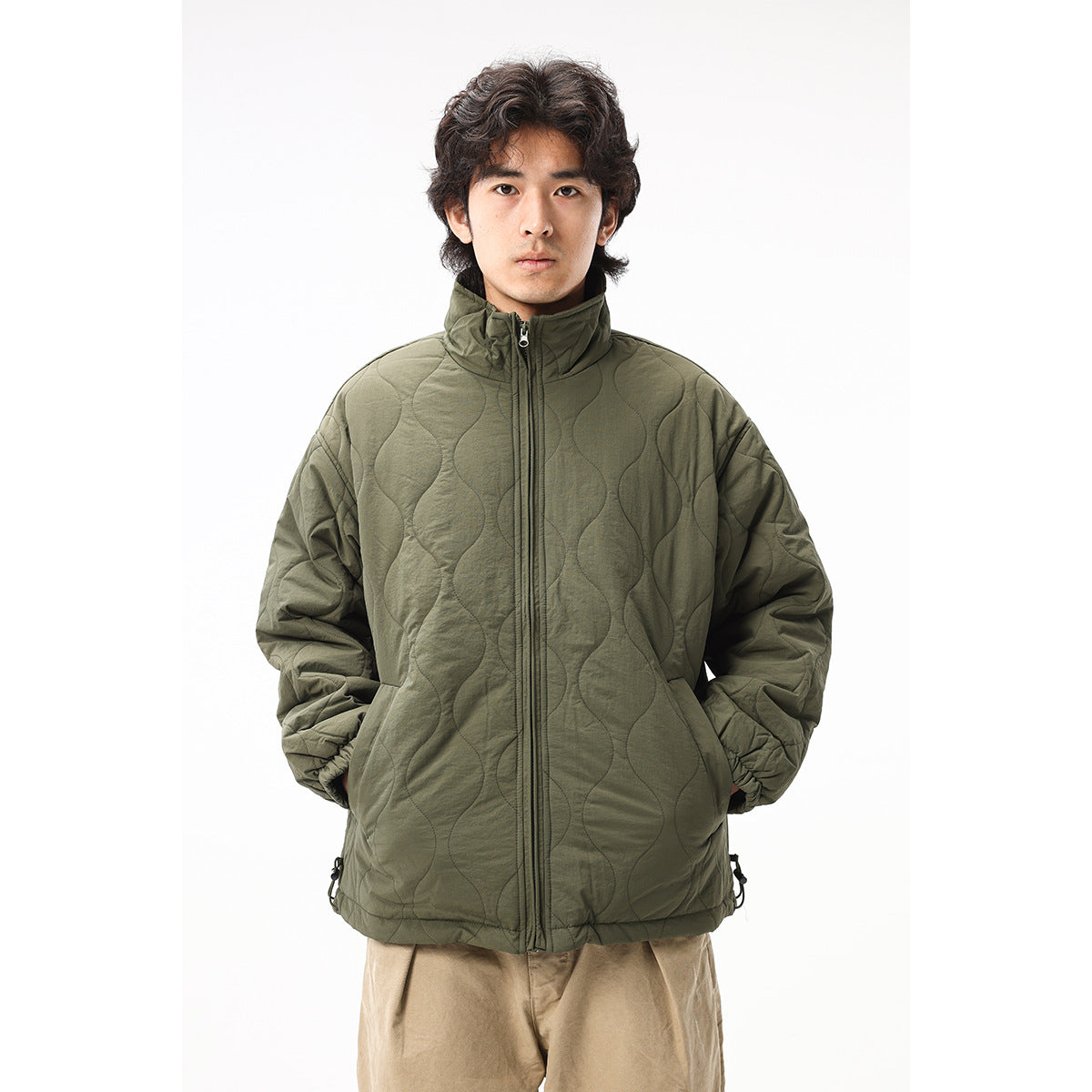 Man wearing an olive quilted zip jacket with a high collar, elastic cuffs and side pockets, shown from the front.