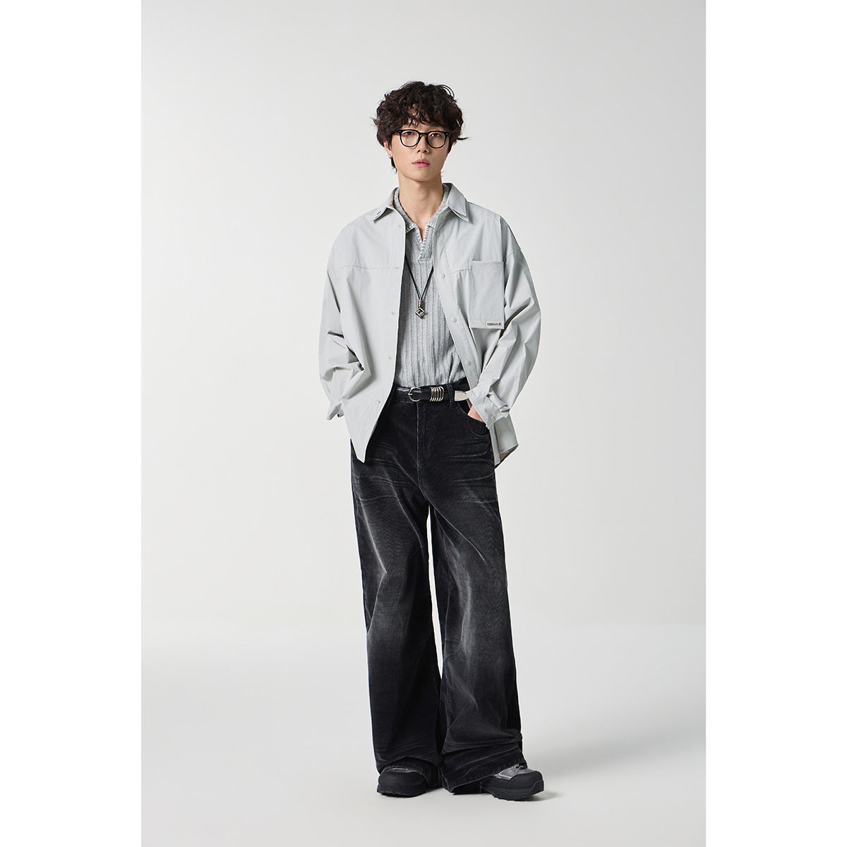 Model wearing a light gray oversized button-front shirt over a gray knit top and black wide-leg trousers.
