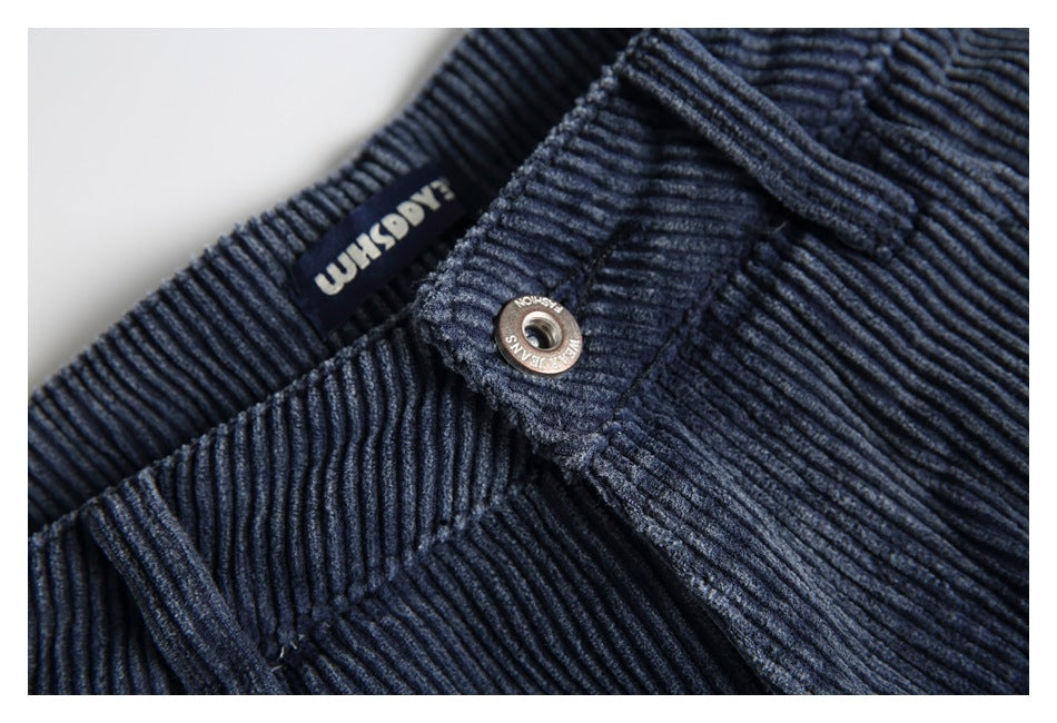 Close-up of the waistband, sewn label and metal button on navy ribbed trousers.