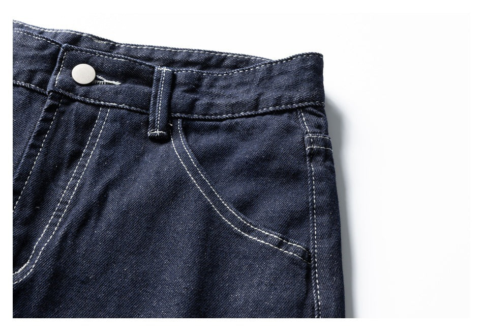 Close-up of dark indigo jeans waistband, metal button, belt loop and curved front pocket.