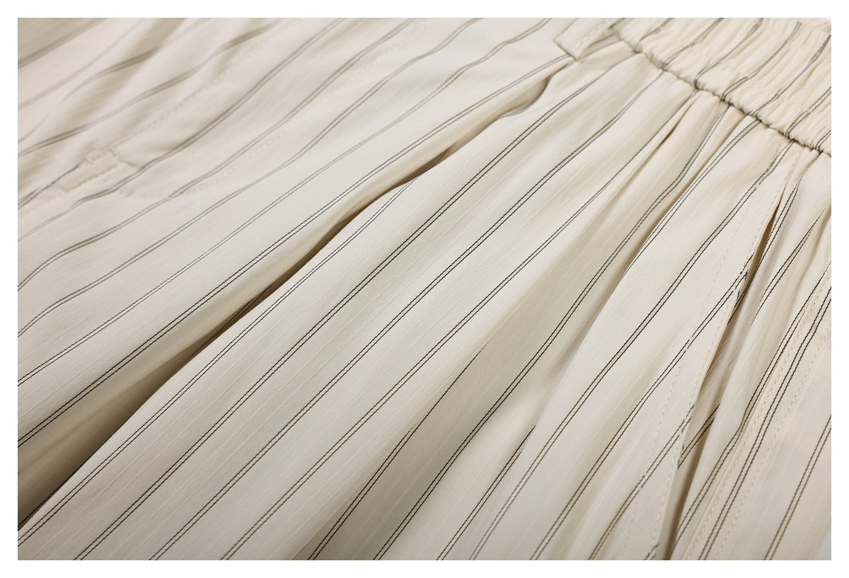 Close-up of the gathered waistband and pleated striped fabric on cream trousers.