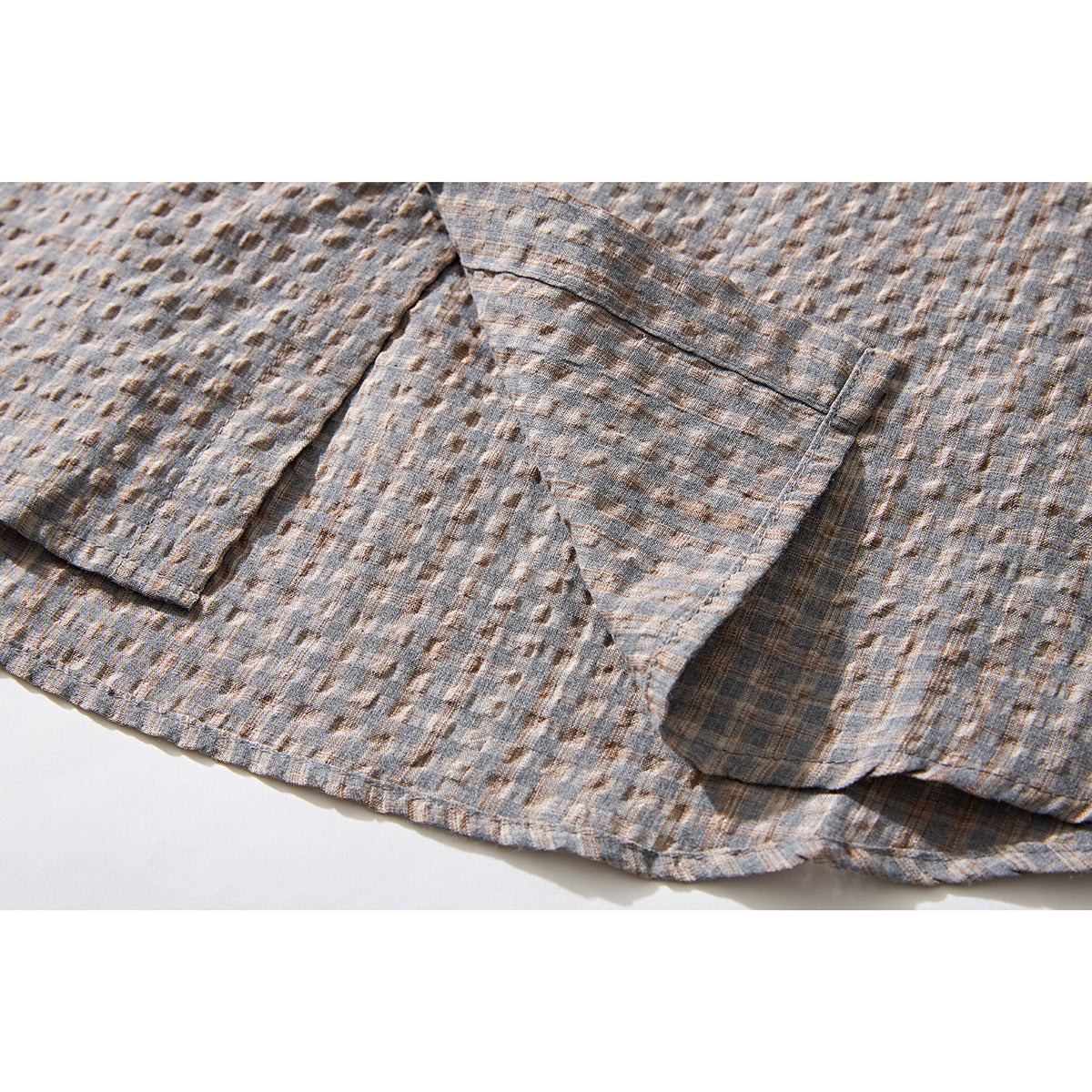 Close-up of a patch pocket and hem on a gray-brown textured plaid shirt.