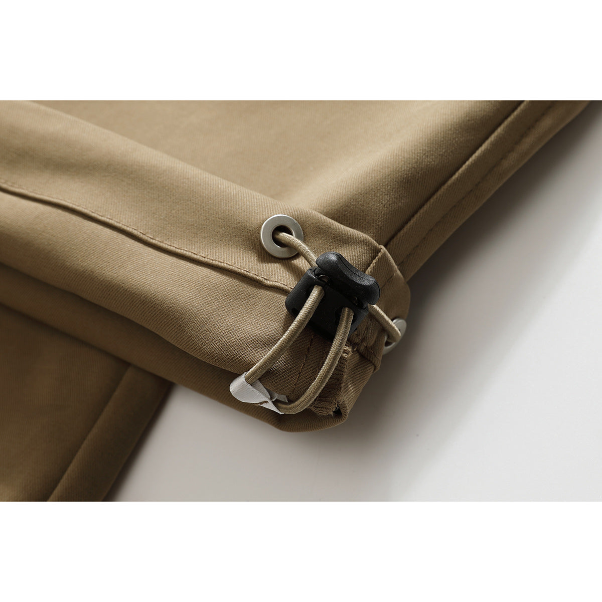 Close-up of the tan pants’ hem with a metal eyelet, drawcord, and black cord lock.