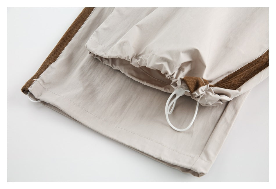 Close-up of a gathered opening with a white drawcord on light beige trousers with brown side trim.