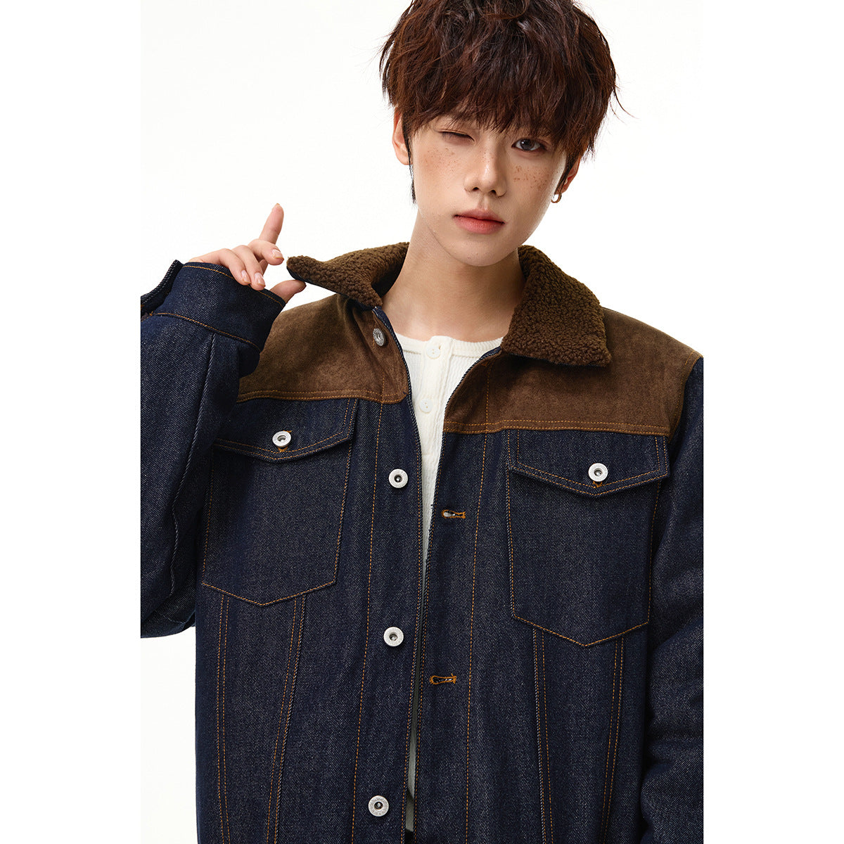 Close view of a model wearing a dark denim jacket with brown shoulder panels, sherpa collar, and buttoned chest pockets.