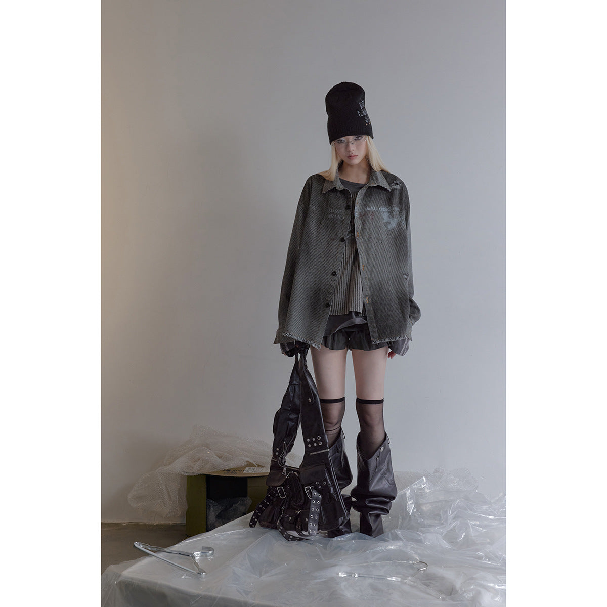 Full-length model wearing an oversized charcoal pinstriped jacket, black beanie, shorts and tall boots.