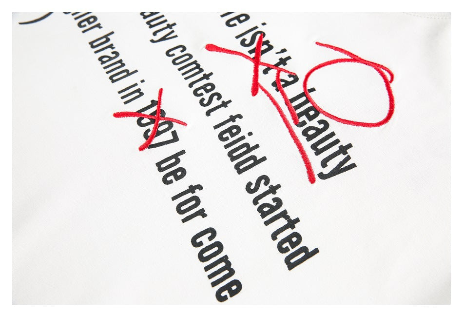 Angled close-up of black English text with red embroidered marks on white fabric.