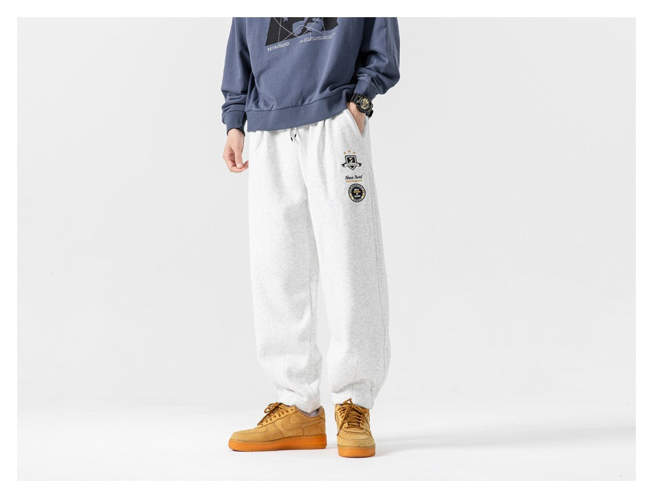 Model wearing heather gray sweatpants with embroidered badges, blue sweatatop and tan sneakers, front view