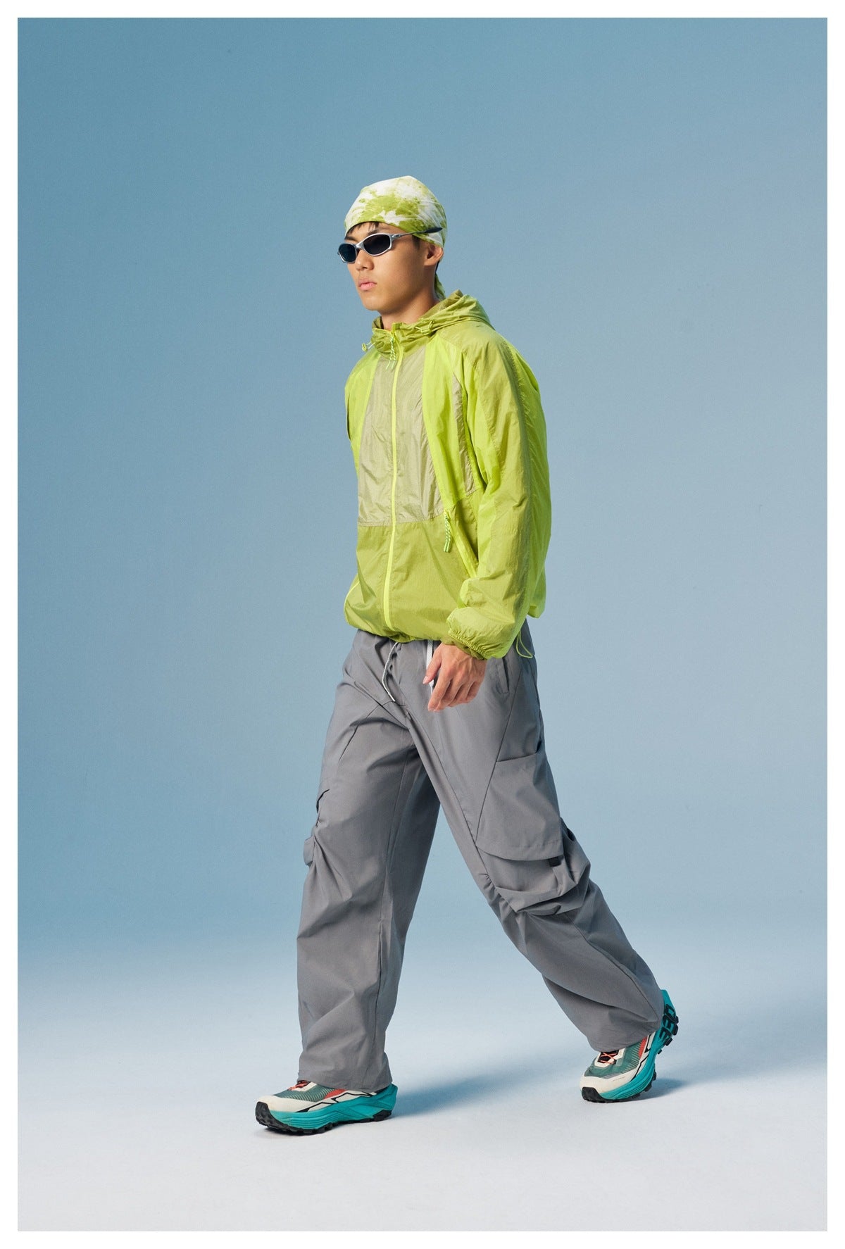 Model wearing a lime-green color-block hooded jacket with gray cargo pants, patterned headscarf, and sunglasses.