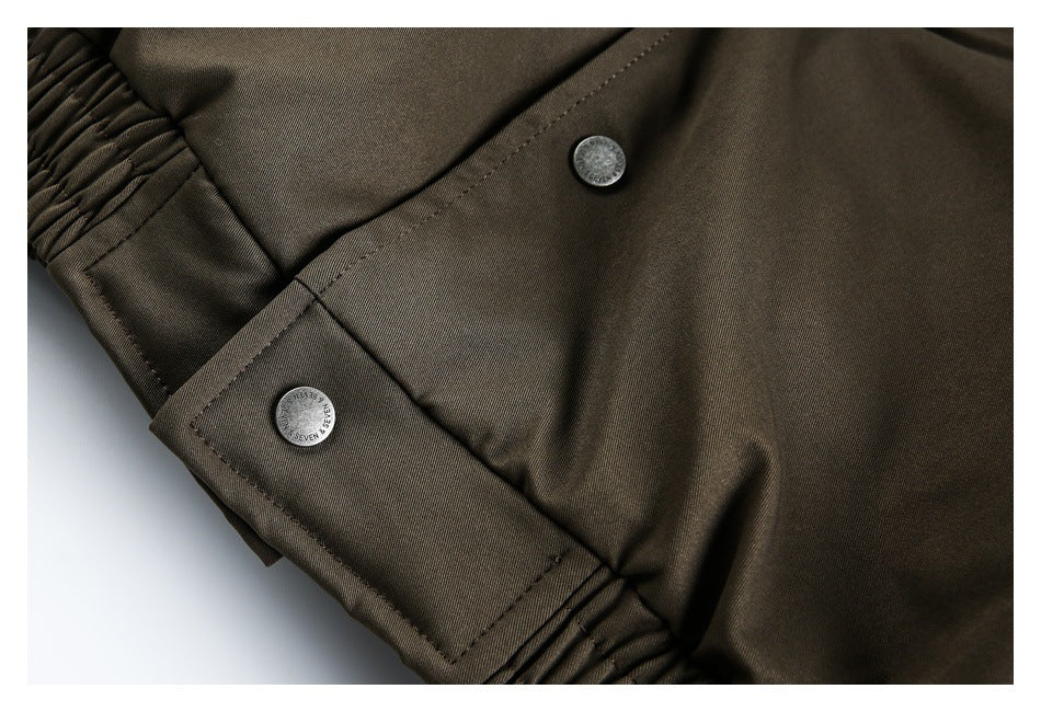 Close-up of an olive-brown garment with two silver snap buttons and gathered stitching.