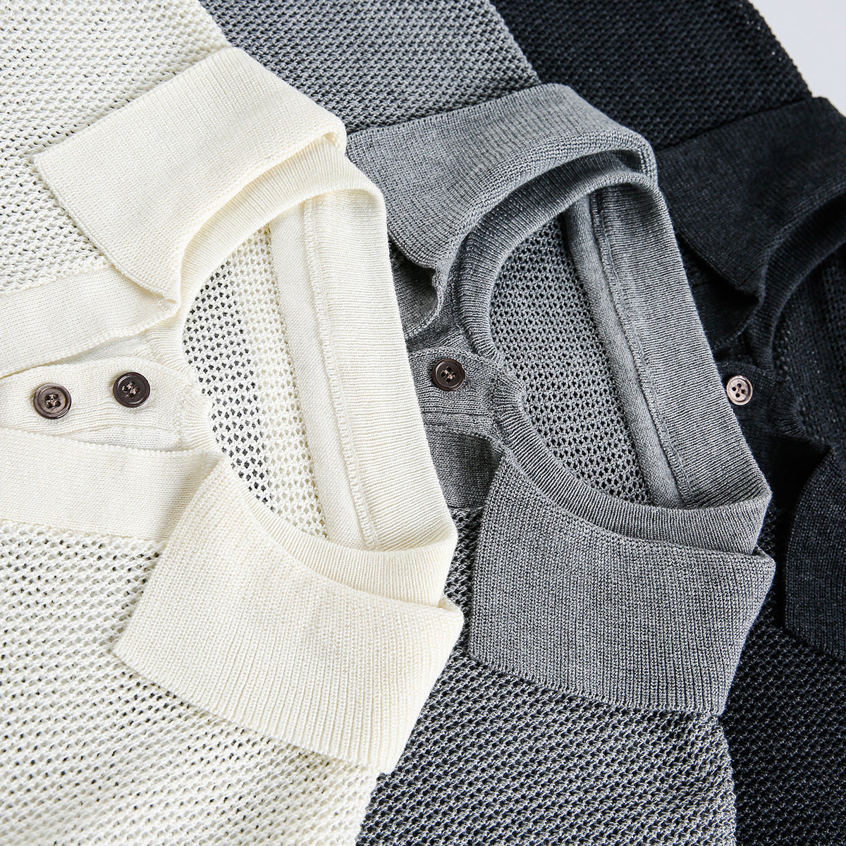 Close-up of three knit polo shirts in ivory, gray, and black, showing collars, button plackets, and open-knit texture.
