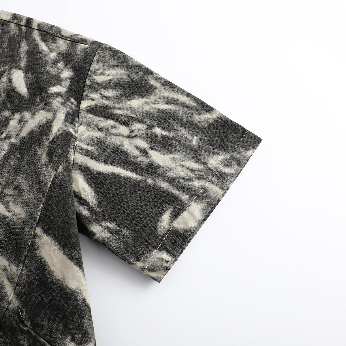 Close-up of the short sleeve and shoulder seam on a black and cream abstract-patterned shirt.