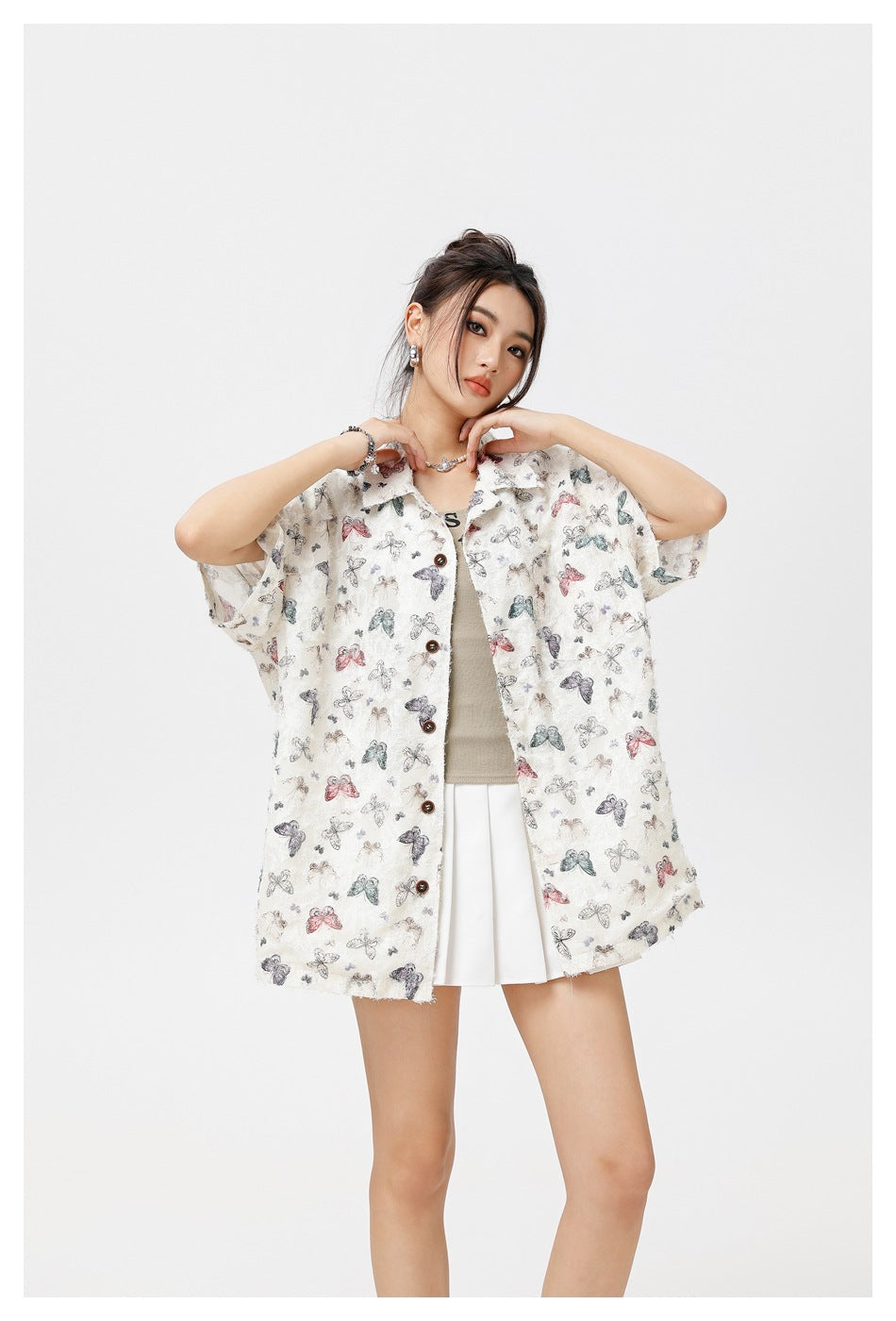 Model wearing an oversized cream short-sleeve button-up shirt with a multicolor butterfly print over a white skirt.