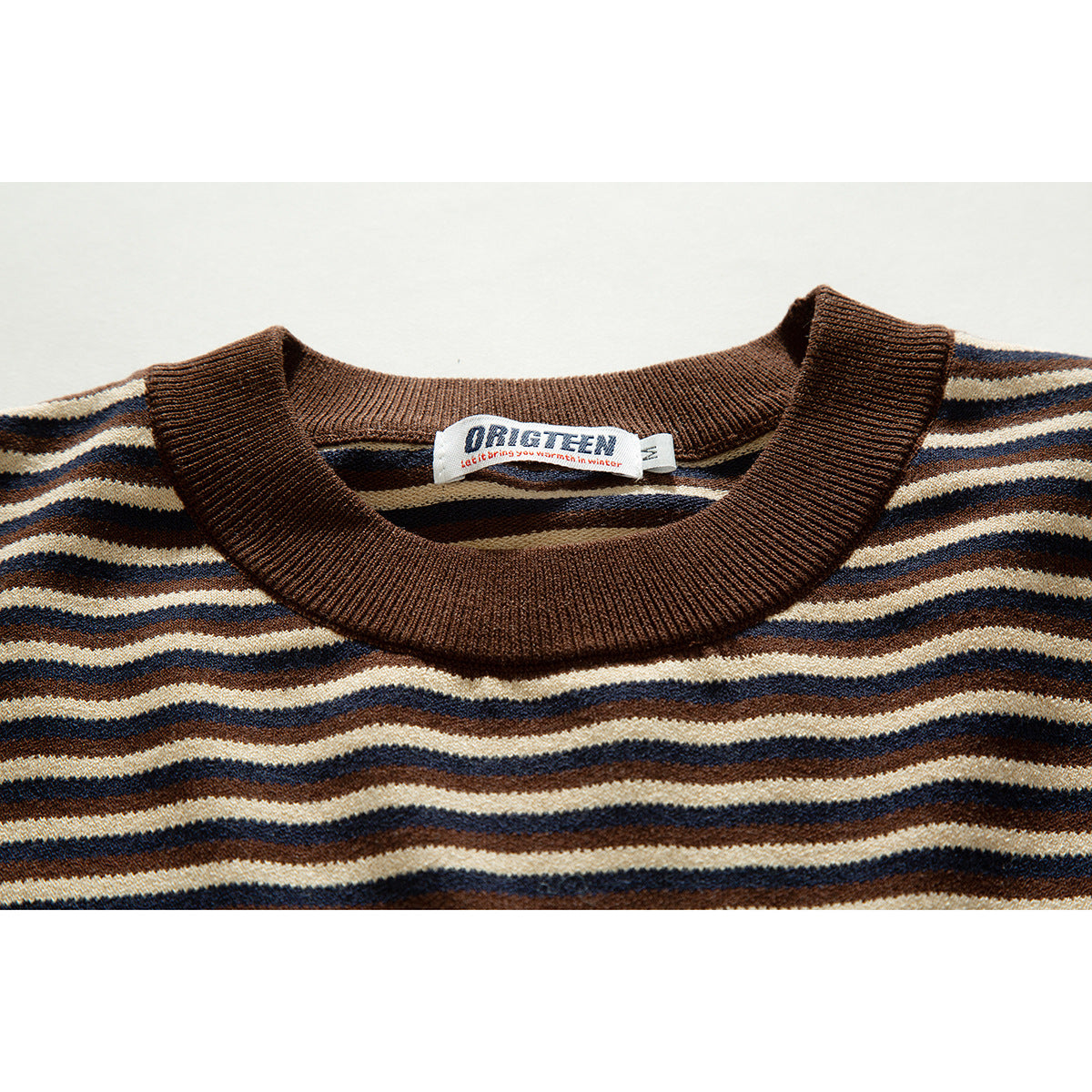 Close-up of a brown ribbed crew neck and cream, brown, and navy horizontal stripes with a sewn neck label.