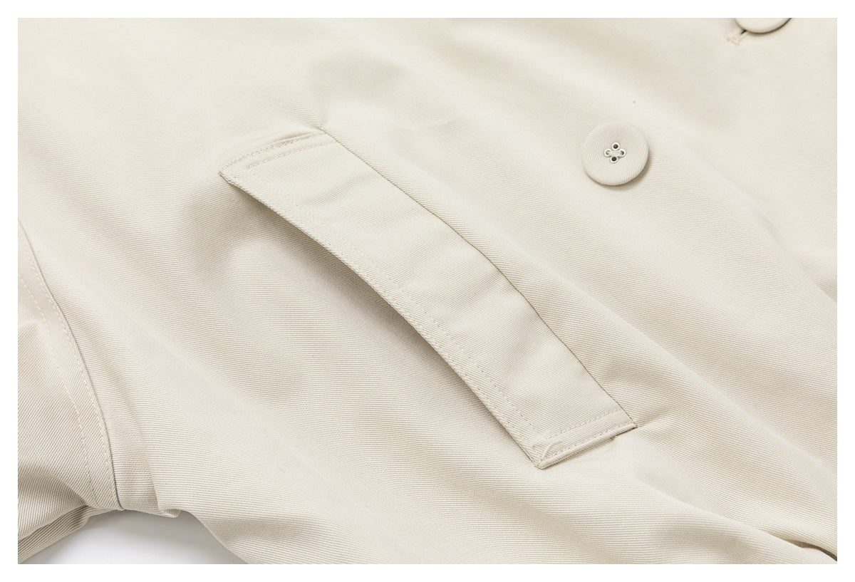 Close-up of a long stitched strap across the light beige coat, beside a matching button.