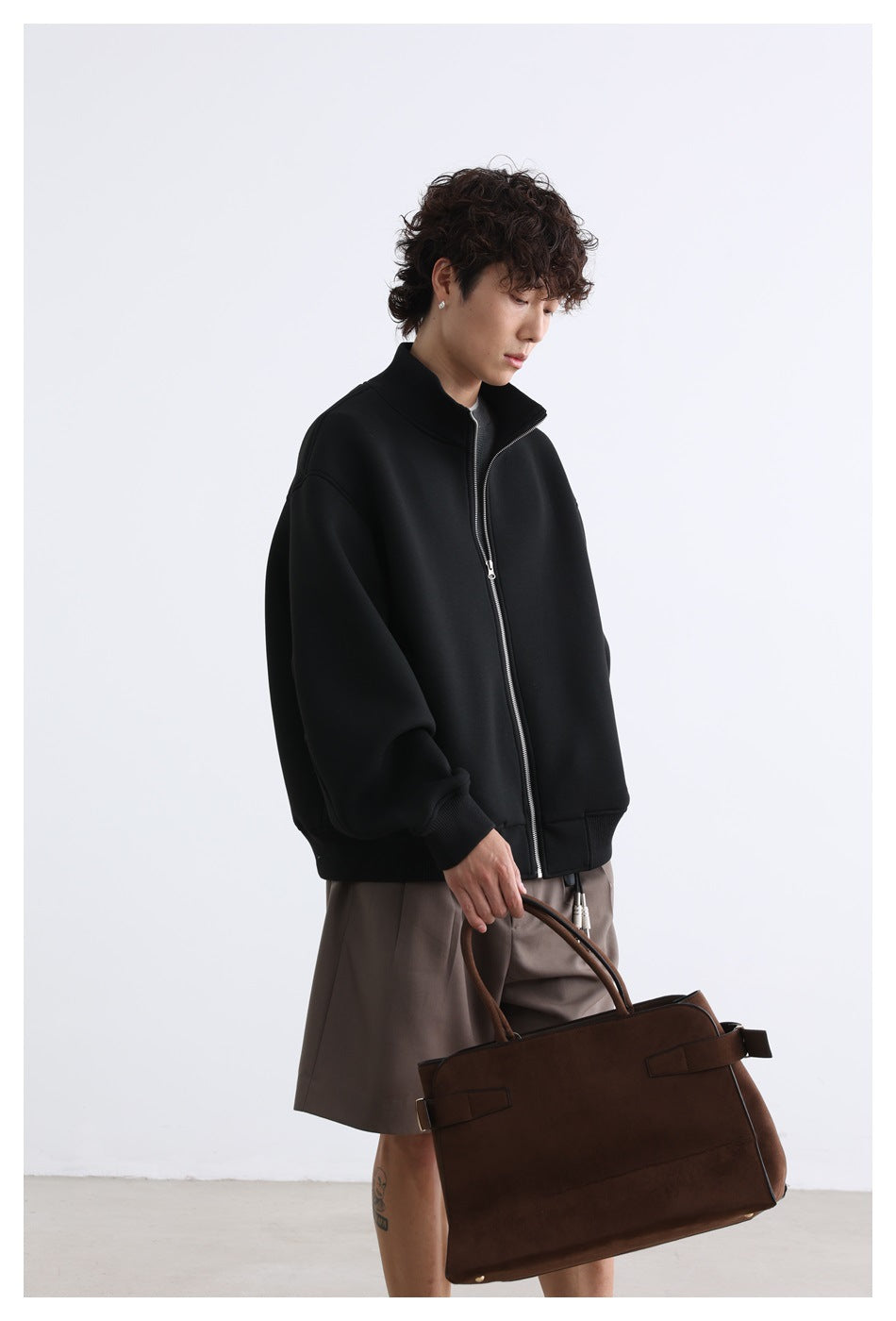 Angled view of a model wearing a black zip jacket with a raised collar and ribbed cuffs.