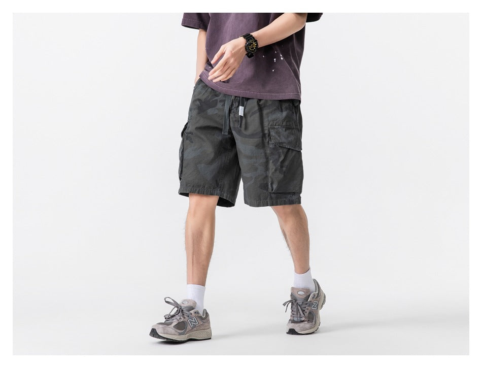 Angled front view of a model wearing dark charcoal camouflage cargo shorts with a drawstring waist and cargo pockets.